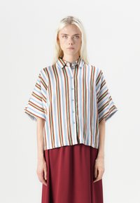 Blusa a maniche corte a righe, con linee verticali in rosso, blu e bianco, dotata di chiusura a bottoni frontale e una vestibilità comoda. Tessuto morbido.