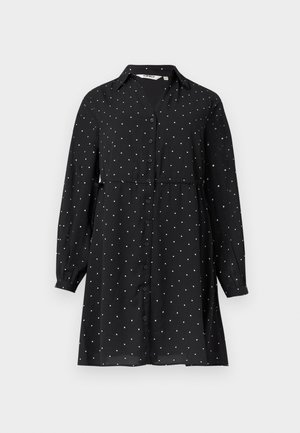 Musta pitkähihainen nappilista mekko, jossa on valkoisia pilkkuja, kauluksellinen pääntie, vyötärö kiristetty ja hieman levenevä helma.