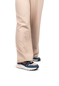 Zapatillas azules y beige con un upper de tela texturizada, cordones y una suela blanca gruesa, llevadas con pantalones beige de pierna ancha.
