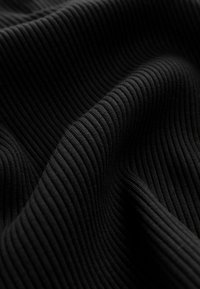 Tejido negro acanalado que muestra líneas verticales prominentes y una textura suave, con pliegues sutiles que resaltan su flexibilidad y profundidad.