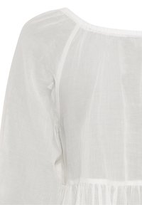 White linen blouse featuring a relaxed fit, long sleeves, a wide neckline, and a textured surface with gathered detailing at the hem.