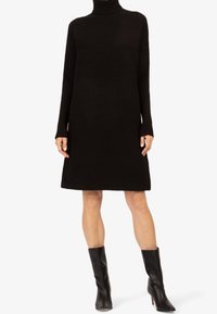 Robe en tricot noir à col roulé avec texture côtelée, manches longues et silhouette A-line ample, associée à des bottines noires brillantes.