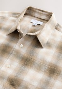 Bézs és barna kockás ing, gombos gallérral, egyetlen mellzsebbel és texturált anyaggal. Fehér "NEXT" feliratú címkével.