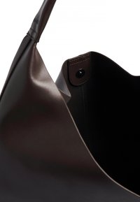 Mörkbrun läderhandväska med en bred öppen topp, som visar en sydd knappknäppning på insidan.