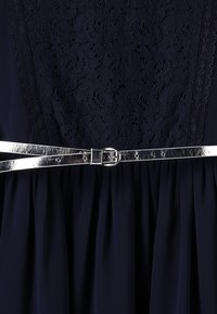 Námořnické šaty s texturovaným krajkovým živůtkem, nařasenou sukní a kovovým stříbrným páskem s kulatou sponou pro detail a strukturu.