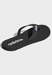 Chancla negra con suela plana, tiras de goma y logo blanco de Adidas en la tira superior. Diseño simple y minimalista.