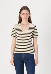 Stripet kortermet t-skjorte med v-hals, laget av bomull i beige farge med marineblå striper, og en liten logo på brystet.