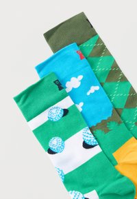 Τρεις χρωματιστές κάλτσες με μοτίβα εμπνευσμένα από το γκολφ: μπάλες γκολφ σε πράσινο και λευκό, γαλάζιος ουρανός με σύννεφα και πράσινο σχέδιο argyle με δέντρα.