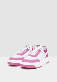 Baskets de sport blanches avec des accents en daim rose. Les caractéristiques incluent une pointe ronde, des lacets plats et une épaisse semelle en caoutchouc blanche. Marquage sur la languette.