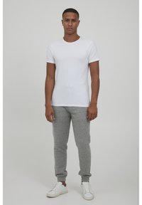White short-sleeve t-shirt, grey jogger pants, and white sneakers. The outfit features a casual design with a fitted shape and plain textures.