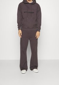 Tmavě šedá mikina s kapucí a černým logem, doplněná vhodnými širokými kalhotami, vyrobená z měkkého materiálu, doplněná bílými teniskami.