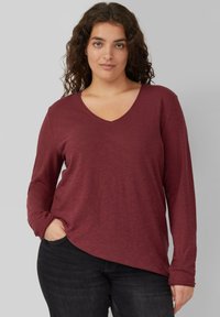 Langärmliges, V-Ausschnitt T-Shirt in kastanienbraun, aus einem weichen, strukturierten Stoff gefertigt. Das Shirt hat eine lockere Passform und einen seitlichen Schlitz am Saum.