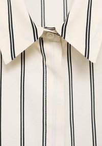 Kraagshirt van crèmekleurige stof met verticale zwarte strepen, voorzien van een knoopsluiting en een soepele textuur, die de eenvoud van het ontwerp benadrukt.
