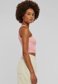 Vaaleanpunainen ribattu crop-top, jossa on ohuet hihnat, yhdistettynä vaaleanvärisiin elastiseen vyötäröön varustettuihin collegehousuihin, joissa on sivutaskut. Pehmeä puuvillakangas.