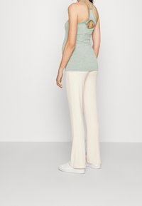 Light green, sleeveless top with a racerback design and a circular cutout. Paired with cream-colored, flared, ribbed pants. White sneakers.