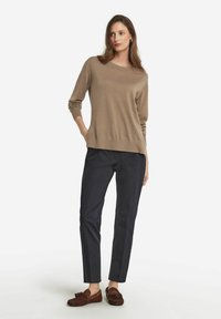 Brun tröja, marinblå byxor och bruna mockasiner. Tröjan har en rundad hals och ribbade ärmslut; byxorna har smal passform med rak ben.