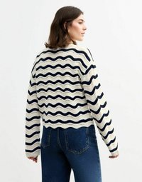 Krämfärgad tröja med marinblå vågiga ränder, kort design, ribbade ärmslut och strukturerad stickning. Kombinerad med högmidjade blå jeans.