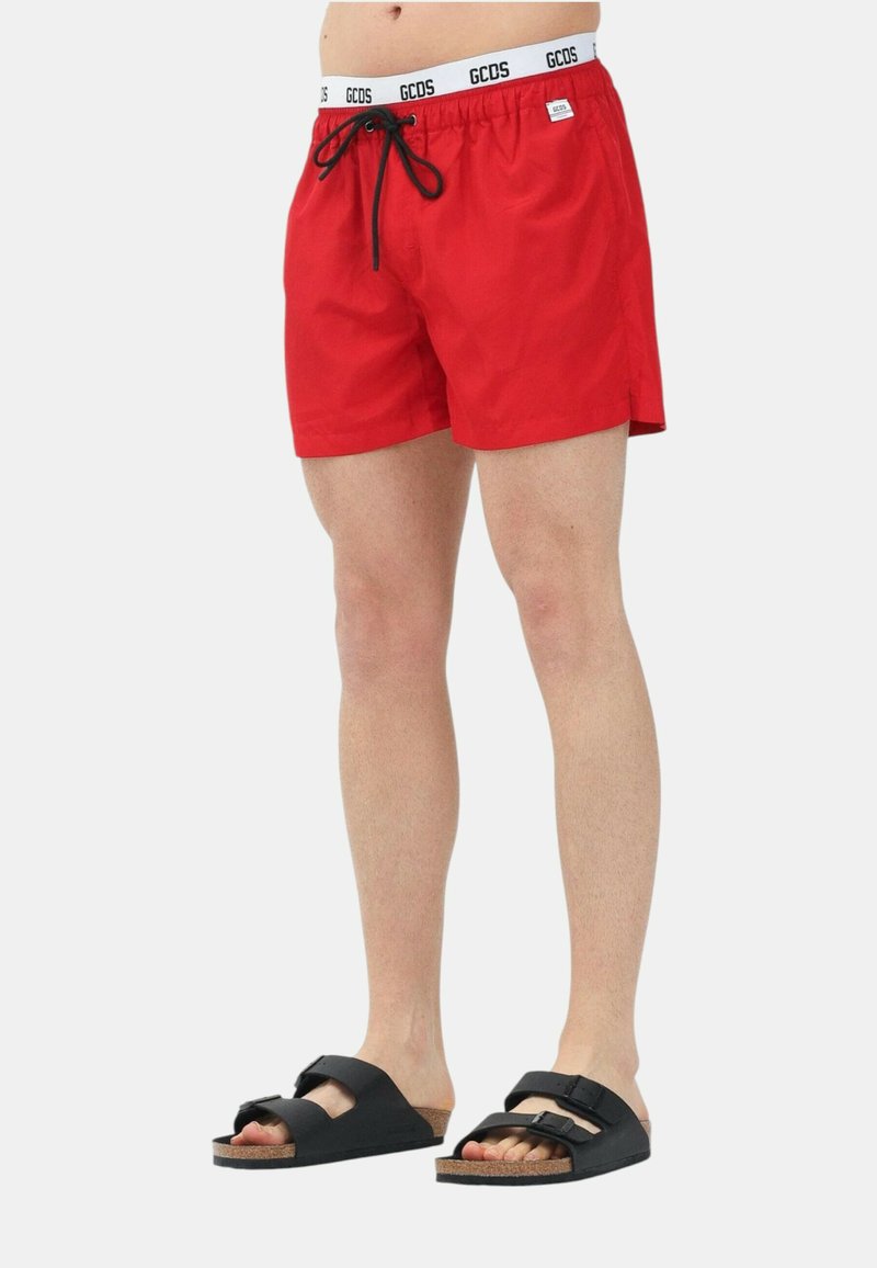 Pantaloni da bagno rossi con vita elastica e cordino, con il logo GCDS. Abbinati a sandali neri con due fasce regolabili.