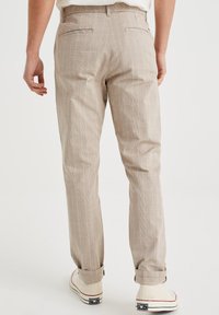 Beżowe spodnie w paski o dopasowanym kroju, z tylnymi kieszeniami i podwiniętymi mankietami, wykonane z lekkiego materiału. Casualowe płaskie buty.