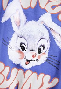Hvit tegneseriekaninansikt med rosa detaljer på en blå bakgrunn. Teksten under leser "Bunny" i leken oransje skrift. Myk tekstur, livlig design.