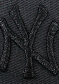 Black fabric featuring an embossed black New York Yankees logo with a thick, textured embroidery, set against a smooth, woven background.