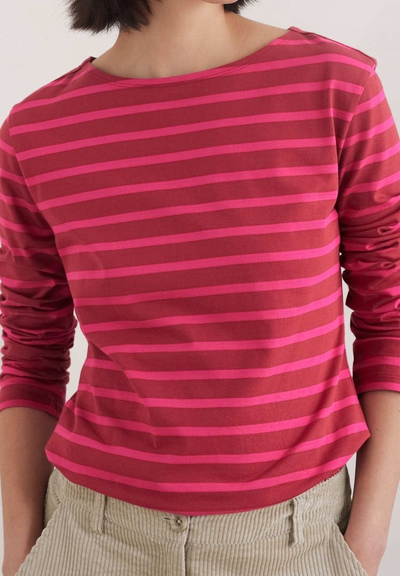 Röd långärmad skjorta med horisontella rosa ränder, rund halsdesign och mjukt tyg. Kombinationen med ljusa kordbyxor.