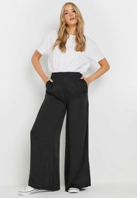 Pantalons larges en lin noir avec une taille élastique, dotés de poches latérales. Associés à un t-shirt blanc à col rond uni et des baskets blanches.