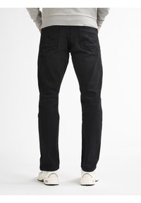 Zwarte denim jeans met een slim fit, voorzien van gestikte achterzakken, een eenvoudige tailleband en een gladde textuur. Draagt met lichtgekleurde sneakers.