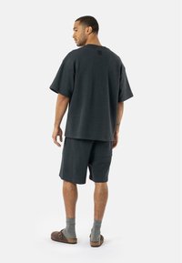 T-shirt oversize en coton gris foncé et shorts assortis, tissu texturé, coupe décontractée, porté avec des sandales marron et des chaussettes grises, poche à la taille visible.