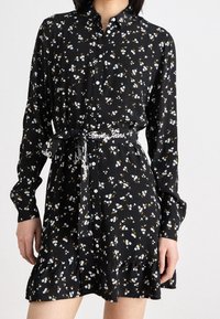 Černé šaty s knoflíky a květinovým potiskem v modré a žluté barvě, s volánkovým lemem a vázacím páskem s brandingem "Tommy Jeans".
