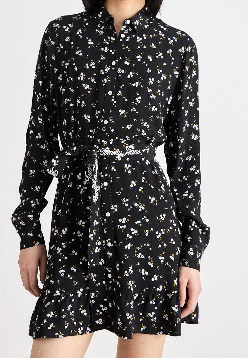 Černé šaty s knoflíky a květinovým potiskem v modré a žluté barvě, s volánkovým lemem a vázacím páskem s brandingem "Tommy Jeans".