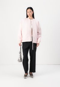 Lys rosa bomberjakke med ribbestrikkede mansjetter, svarte vidde bukser, metallisk håndveske og sølv loafers. Enkel, moderne design.