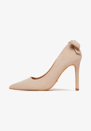 Bēšas zamšādas augstpapēžu kurpes ar smailu purngalu un loku akcentu aizmugurē. Aprīkotas ar plānu stiletto papēdi un gludu tekstūru.