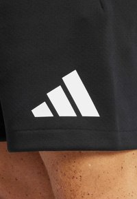 Shorts neri con un prominente logo bianco Adidas e tre strisce diagonali, realizzati in un tessuto morbido ed elasticizzato per il massimo comfort.