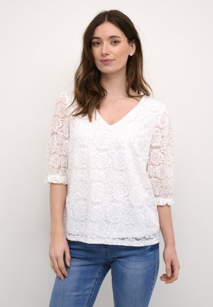 Vit spetsblus med V-ringning, ärmlängd puffärmar, blommönster och lös passform. Matchas med blå jeans.