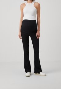 Svarta utsvängda byxor med en mjuk struktur, hög midja och en figursydd vit ribbad linne. Outfiten kombineras med vita sneakers.