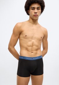 Μαύρα βαμβακερά μπόξερ με μπλε μέση που διαθέτει τη φράση "TOMMY HILFIGER" και λογότυπο. Ομαλή υφή, εφαρμοστή σχεδίαση και μεσαία εφαρμογή.