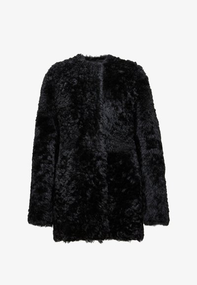 Melnā mākslīgā kažokā ar teksturētu, pusgaru izskatu. Tam ir noapaļota apkakle un nav redzamu aizdaru, nodrošinot brīvu piegriezumu.