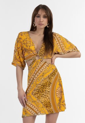 Geel-gepatroniseerde jurk met korte mouwen, V-hals en uitsnijding. Bevat dierenprint, barokke patronen en een getailleerde taille.