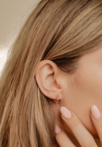 Boucles d'oreilles en or avec un design de maillons de chaîne. Texture lisse et petite taille, complétant les cheveux droits et clairs ainsi que les ongles naturels.