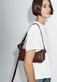 Borsa a tracolla in pelle marrone con una superficie liscia, forma rettangolare, accessori in metallo argentato e una lunga tracolla da indossare sulla spalla.