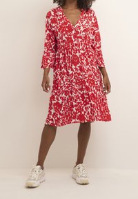 Abito floreale rosso con scollatura a V, maniche a tre quarti e gonna arricciata. Realizzato in tessuto leggero, presenta un motivo floreale bianco.