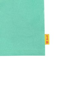 Camiseta de algodón verde menta con una textura suave, dobladillo recto y una etiqueta amarilla con un logo de oso en la costura lateral.