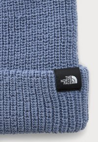 Lyseblå ribbet strikhue med ombuk og sort syet label, der viser The North Face-logoet i hvid.