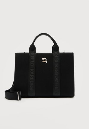 Μαύρη ορθογώνια τσάντα tote με δύο χερούλια, ρυθμιζόμενο λουρί ώμου και μια μικρή καρφίτσα με τη φιγούρα ενός ατόμου που φορά γυαλιά ηλίου στο μπροστινό μέρος.