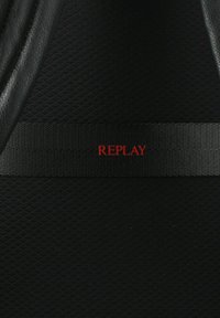 Sfondo nero testurizzato con un nastro orizzontale nero sul quale è scritto "REPLAY" in rosso. Il materiale appare liscio e resistente.