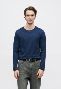 Tumesinise värvi pika varrukaga särk kerge kangaga, ümmarguse kaelusega. Sobitatud hallide teksade ja musta vöögiga, klassikalise lõikega.