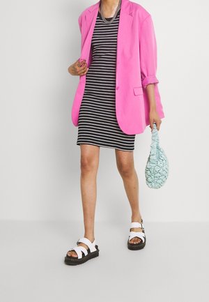 Personne portant une robe rayée noire et blanche, un blazer rose vif, des sandales blanches, tenant un sac à main bleu clair texturé.