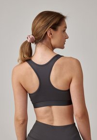 Grijze sportbeha met een racerback ontwerp, gemaakt van soepel materiaal. Heeft brede bandjes en een strakke pasvorm, die de rugvorm accentueert.