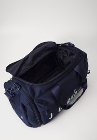Bolsa de lona navy con apertura con cremallera, exterior de tela, asas dobles y un amplio interior negro. Presenta letras blancas en el lateral.